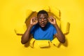 Emotional black man in eyeglasses looking at camera through hole in yellow paper, opening mouth with shock, banner Royalty Free Stock Photo