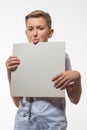 Emotional blond boy in a white shirt with a gray sheet of paper for notes Royalty Free Stock Photo