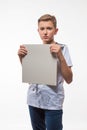 Emotional blond boy in a white shirt with a gray sheet of paper for notes Royalty Free Stock Photo