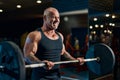 Emotional Older bald sportsman trains in the gym while pumping up biceps muscles with barbell