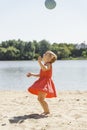 Cute little girl in a red dress plays with a ball on the sand Royalty Free Stock Photo