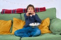 Emotional child watching tv on the sofa and eating popcorn at home, free space