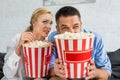 emotional couple holding popcorn boxes while watching tv