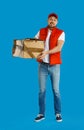 Emotional courier with cardboard box on blue background. Poor quality delivery service Royalty Free Stock Photo