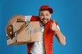 Emotional courier with damaged cardboard box on blue. Poor quality delivery service Royalty Free Stock Photo