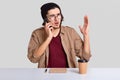 Emotional displeased guy has telephone coversation, raises hand, discusses something actively, drinks takeaway coffee, sits at