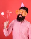 Emotional diversity concept. Man with beard on cheerful face holds smiling lips on sticks, red background. Guy in party Royalty Free Stock Photo
