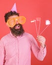 Emotional diversity concept. Man with beard on cheerful face holds smiling lips on sticks, red background. Guy in party Royalty Free Stock Photo