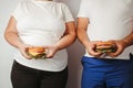 Overweight couple snacking with hamburgers