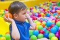 An emotional face of smiling baby playing in the balls pool. Happy kid playing with colored balls. Child playing with colorful bal