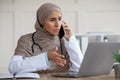 Emotional female doctor looking at laptop screen, talking on phone Royalty Free Stock Photo