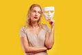 Emotional female person with white mask on yellow background. Internet fraud concept, anonymous, incognito, bipolar personality di