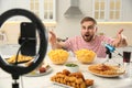 Emotional food blogger recording eating show on smartphone camera in kitchen. Mukbang vlog Royalty Free Stock Photo