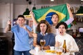 Emotional friends, football fans cheering for favorite Brazil team together while watching match on tv in bar