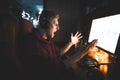 Emotional gamer looks at the computer screen with an evil look, playing games at home in a cozy room