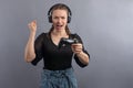 Emotional gamer woman playing video game and using joystick and headphones on grey background. Gambler concept. Using modern