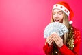 Emotional girl in a red sweater and Santa Claus hat, in admiration holding money on a red background. Royalty Free Stock Photo