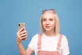 Emotional girl with a smartphone in her hands on a blue background looks at the camera with astonishment. Closeup portrait of a Royalty Free Stock Photo