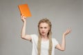 Emotional girl with weaving on her head waving an orange notebook, surprise and doubt of young girl