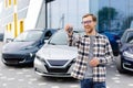 Emotional guy holding key in hand and smiling at camera. Man showing key from his new electric car. Young man buying auto at Royalty Free Stock Photo