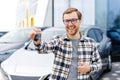 Emotional guy holding key in hand and smiling at camera. Man showing key from his new electric car. Young man buying auto at Royalty Free Stock Photo