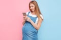 Happy young pregnant woman using a mobile phone looks at the smartphone screen Royalty Free Stock Photo