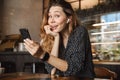 Emotional happy beautiful young pretty woman sitting in cafe indoors using mobile phone talking with friends take a selfie Royalty Free Stock Photo
