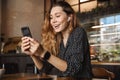 Emotional happy beautiful young pretty woman sitting in cafe indoors using mobile phone talking with friends take a selfie Royalty Free Stock Photo