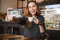 Emotional happy beautiful young pretty woman sitting in cafe indoors using mobile phone talking with friends take a selfie Royalty Free Stock Photo