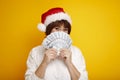 Emotional happy mature middle aged woman in red Santa Claus hat holding money on yellow background. Christmas, business concept Royalty Free Stock Photo