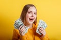 Emotional happy teenage blonde girl win money cash holding dollars in hands isolated on color yellow background. Portrait young Royalty Free Stock Photo