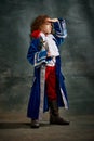 Emotional kid, little girl wearing costume of prince, musketeer and royal person posing over dark vintage style