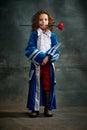 Emotional kid, little girl wearing costume of prince, musketeer and royal person posing over dark vintage style