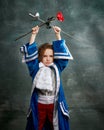 Emotional kid, little girl wearing costume of prince, musketeer and royal person posing over dark vintage style