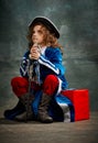 Emotional kid, little girl wearing costume of prince, musketeer and royal person posing over dark vintage style