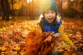 Emotional lifestyle portrait of adorable cheerful baby girl in colorful clothes playing with dry fallen autumn maple leaves in Royalty Free Stock Photo