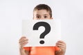 Emotional little boy holding paper with question mark on background Royalty Free Stock Photo