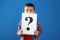 Emotional little boy holding paper with question mark on background Royalty Free Stock Photo