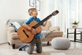 Emotional little boy playing guitar on floor