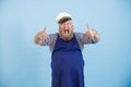 Emotional male person with overweight in sailor suit a shows thumb up on light blue background
