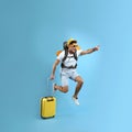 Emotional male tourist with travel backpack and suitcase jumping on turquoise background