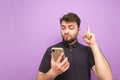 Emotional man with a beard holds a smartphone in his hands, showing his finger up in a blank space.Surprised adult in a dark shirt Royalty Free Stock Photo