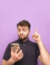 Emotional man with a beard holds a smartphone in his hands, showing his finger up in a blank space. Surprised adult in a dark T- Royalty Free Stock Photo