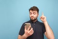 Emotional man with a beard holds a smartphone in his hands, showing his finger up in a blank space. Surprised adult in a dark T- Royalty Free Stock Photo