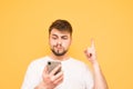 Emotional man with a beard holds a smartphone in his hands, showing his finger up in a blank space. Surprised adult in a white T- Royalty Free Stock Photo