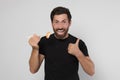 Emotional man holding tasty sushi with chopsticks and showing thumbs up on light grey background