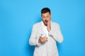 Emotional man looking at smartphone on light blue background. Space for text Royalty Free Stock Photo