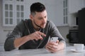 Emotional man with smartphone at table in kitchen. Online hate