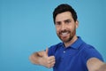 Emotional man taking selfie and showing thumbs up on light blue background, space for text