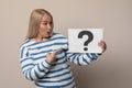 Emotional mature woman holding paper with question mark on beige background Royalty Free Stock Photo